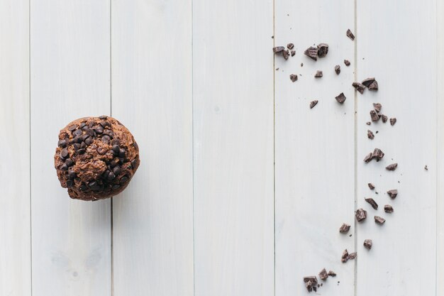 Elevated view of choco chip cupcake and scattered chocolate on wooden background