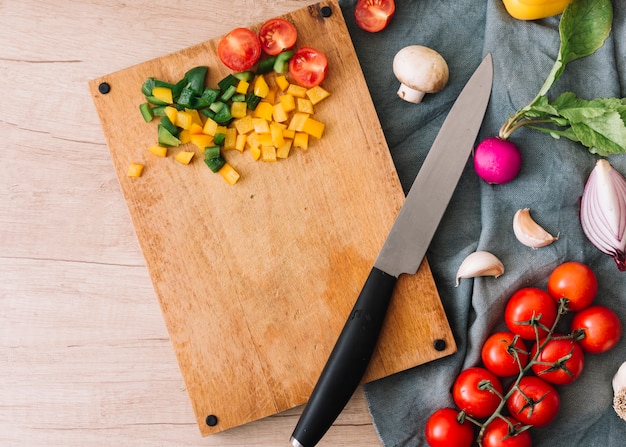 Поднятый вид нарезанных овощей на разделочную доску с ножом над столом