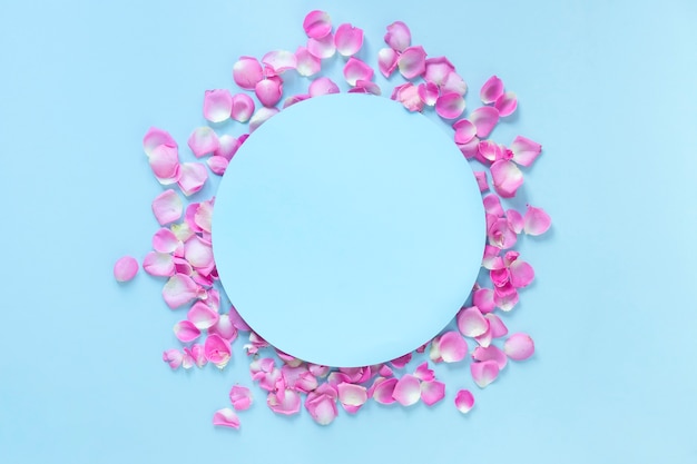 青い背景の上にピンクのバラの花びらに囲まれた円形のフレームの高められた景色