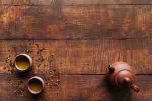 Free photo an elevated view of clay pot with herbal teacups on wooden desk