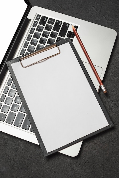 Free photo elevated view of clipboard with blank white paper and pencil on laptop keypad