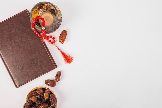 An elevated view of closed diary with prayer beads and fresh dates on white backdrop