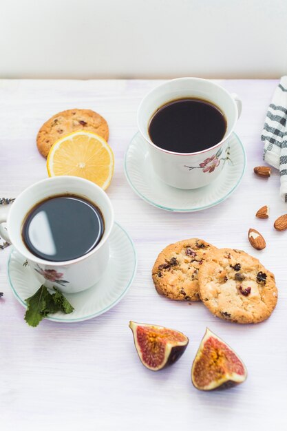 Elevated view of coffee; backed cookies; almond; fig and lemon on wooden table