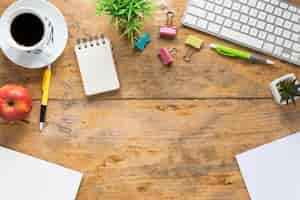 Free photo an elevated view of coffee cup; apple and office stationeries on wooden desk