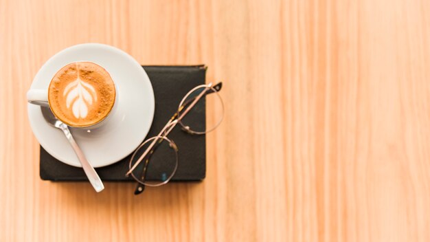 Elevated view of coffee latte and spectacles over book on wooden background