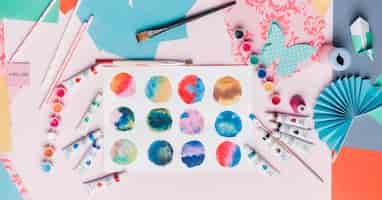 Free photo elevated view of colorful abstract circle painting; straw; origami; and painting equipment