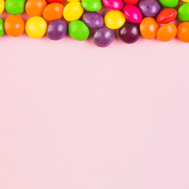 Elevated view of colorful candies at the top of pink background