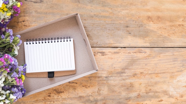 Elevated view of colorful flowers near diary in box on wooden surface