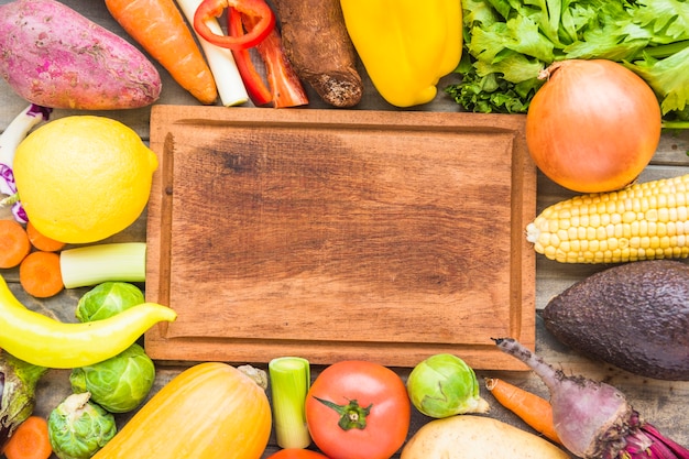 Elevated view of colorful fresh vegetables surrounding wooden chopping board