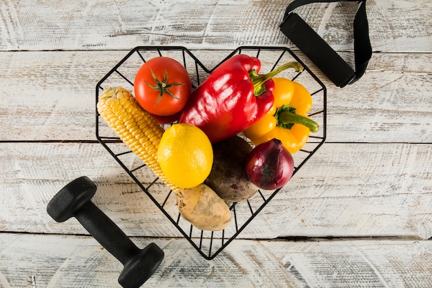 Elevated view of colorful raw vegetables with fitness equipments on wooden background