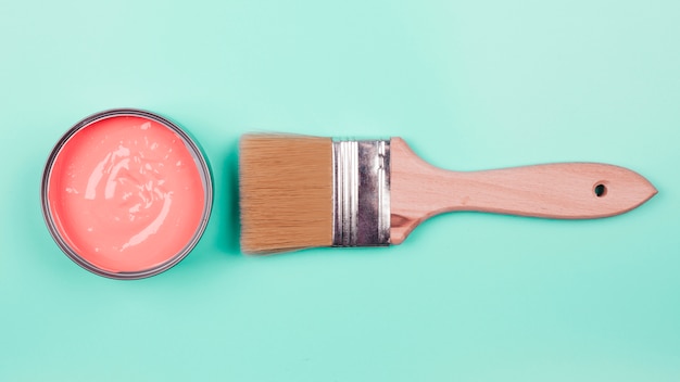 An elevated view of coral paint bucket and paintbrush on mint background