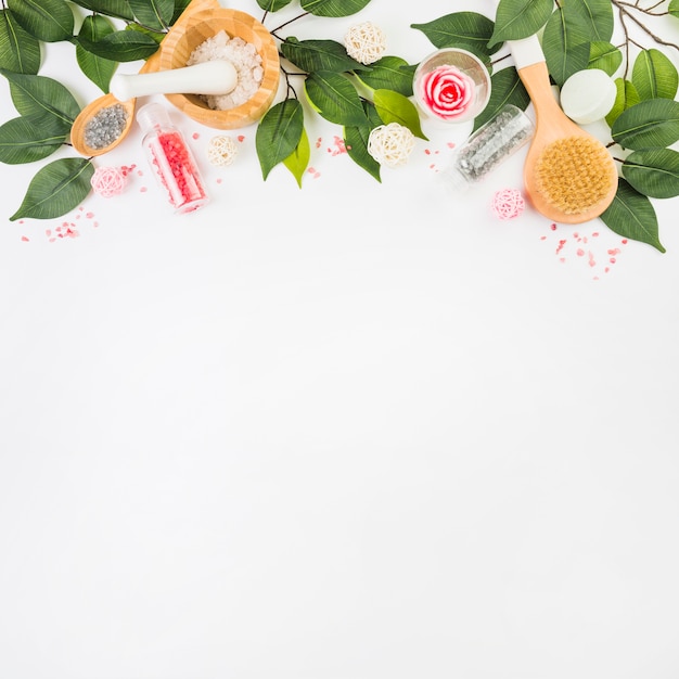 Elevated view of cosmetic products and green leaves at the top of white background