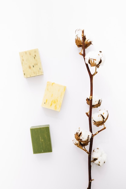 Elevated view of cotton twig with soaps on white surface