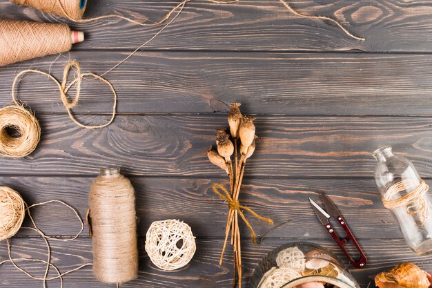 Elevated view of craft material with tied poppy pods and glass bottle