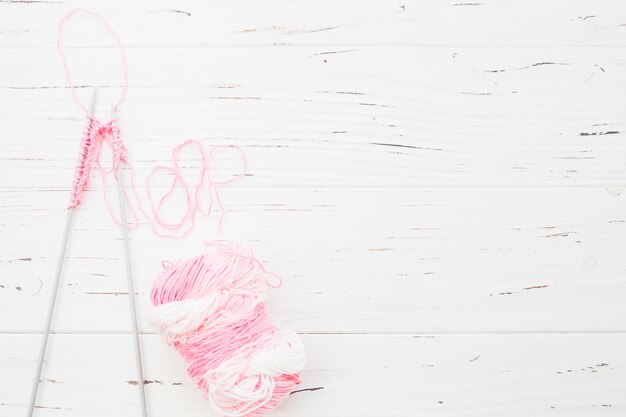 Elevated view of crochet with pink yarn on wooden backdrop