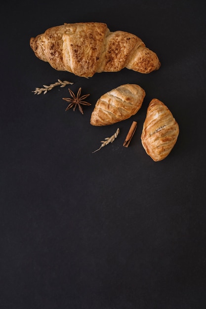 Elevated view of croissants; spices and grains on black background