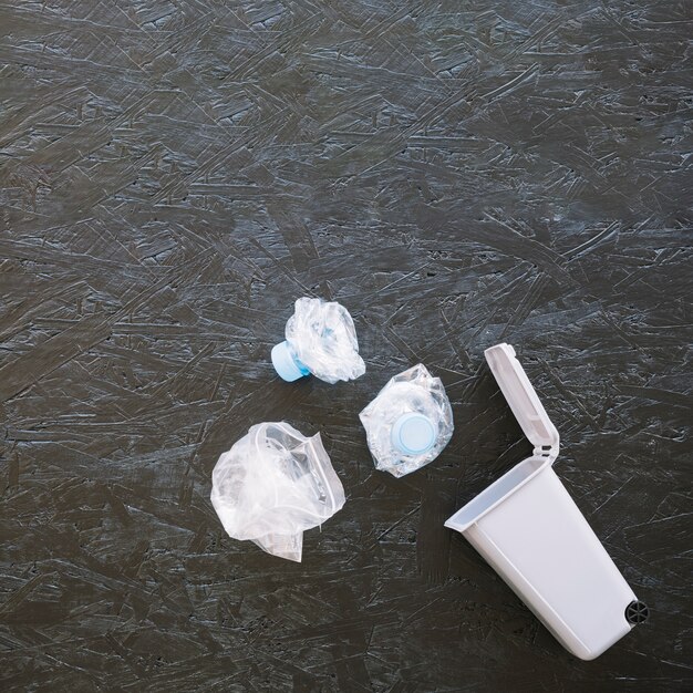 Elevated view of crumpled plastic water bottles near miniature dustbin