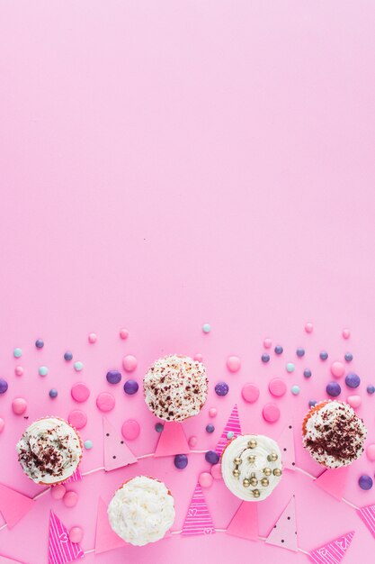 Elevated view of cupcakes; candies and bunting on pink surface