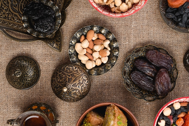 An elevated view of dates; nuts and raisin on metallic bowl over the tablecloth