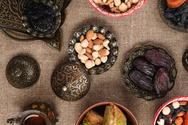 An elevated view of dates; nuts and raisin on metallic bowl over the tablecloth