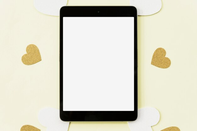Elevated view of digital tablet surrounded with heart sticker on yellow backdrop