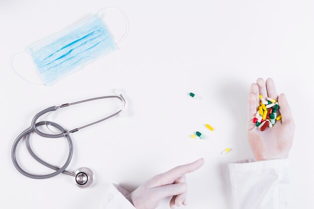 Повышенный вид врача, указывая на красочные капсулы, держа в руке стетоскоп и маска