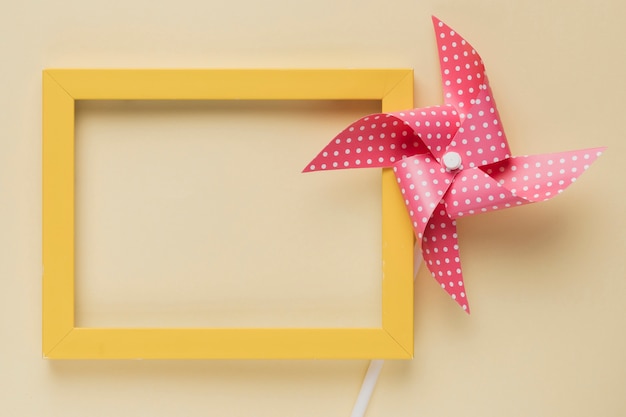 Elevated view of dotted pinwheel and yellow frame on beige background