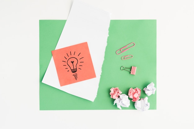 Free photo elevated view of drawn light bulb and crumpled paper with paper clip on green card paper