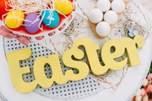 An elevated view of easter text with decorative colorful easter eggs on white table