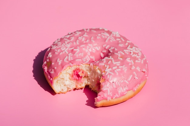 Поднятый вид съеденного пончика на розовом фоне