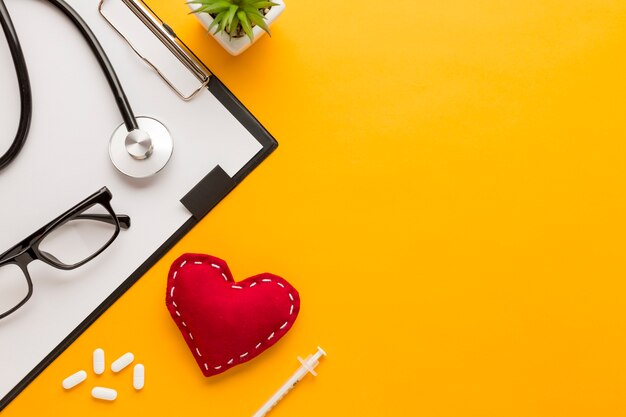 Elevated view of eyeglass; tablet; injection; stitched heart shape; succulent plant; stethoscope over yellow background