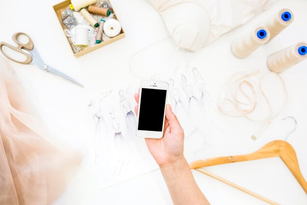 Elevated view of female designer's hand holding smartphone over desk