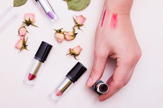 Free photo an elevated view of female hand holding lipstick with dried pink rose buds on white backdrop