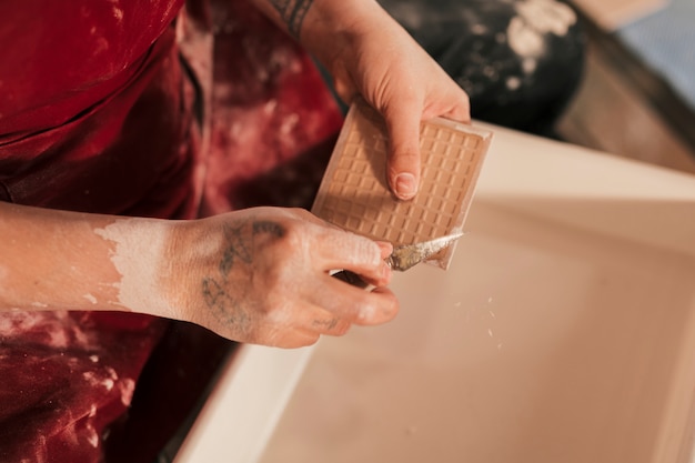 An elevated view of female potter cleaning the paint on tiles with sharp tool