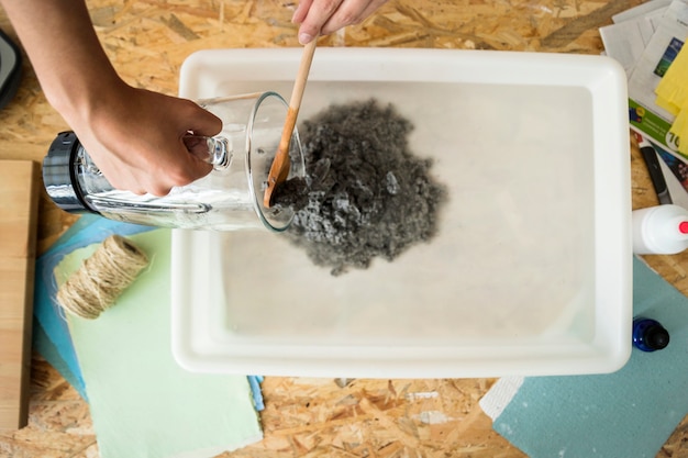 Elevated view of female's hand mixing paper pulp in water