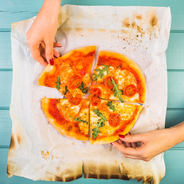 Elevated view of a female's hand picking up vegetable pizza slices