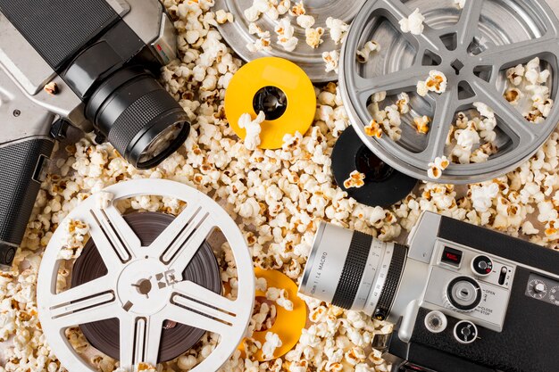 An elevated view of film reel; camera and camcorder over the popcorn