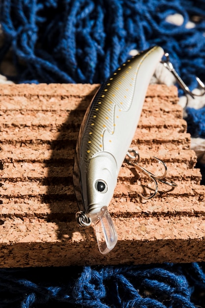 An elevated view of fishing bait with hook on cork board over the blue fishing net