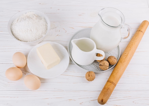 밀가루의 높은 전망; 우유; 달걀; 치즈와 호두 파이 만들기위한 흰색 나무 테이블에