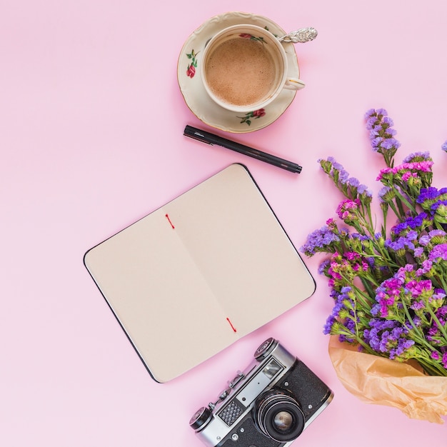 花の花束の高架ビュー。ヴィンテージカメラ;日記;ピンクの背景にペンとコーヒーカップ
