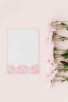 Foto gratuita vista elevata di fiori e carta bianca progettata su sfondo rosa
