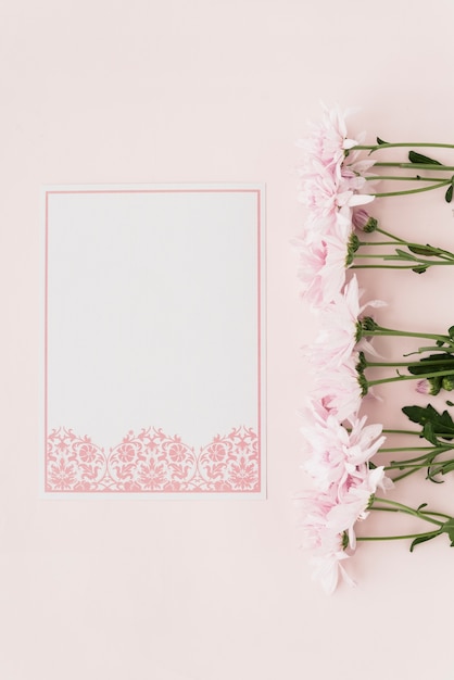 Elevated view of flowers and designed white paper on pink backdrop