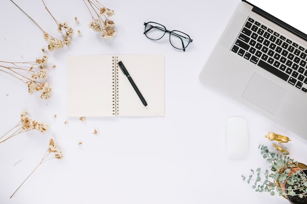 Elevated view of flowers with stationeries and laptop on white desk