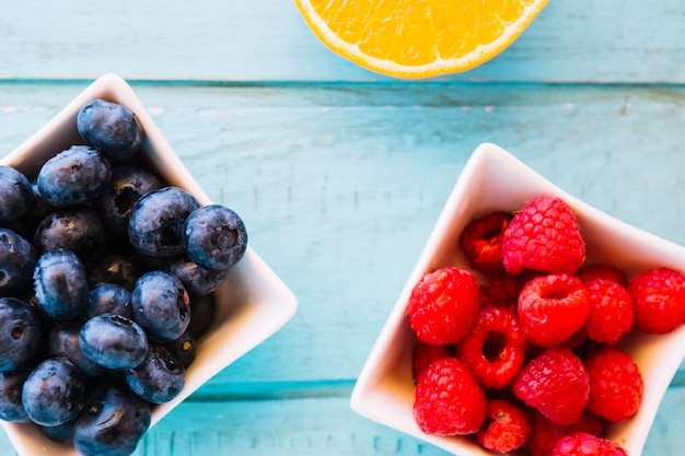 Free photo elevated view of fresh berry fruits in bowl on blue wooden background