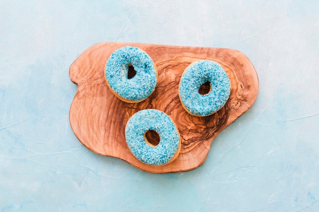 Elevated view of fresh blue donuts on wooden chopping board