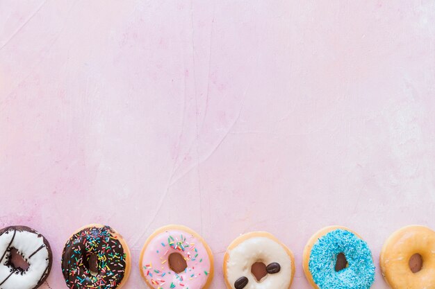 Elevated view of fresh donuts in a row on pink backdrop