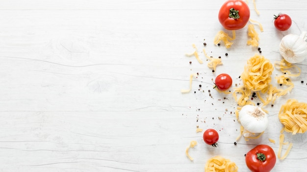 토마토와 신선한 원시 tagliatelle 파스타의 높은보기; 하얀 판자 위에 마늘과 후추