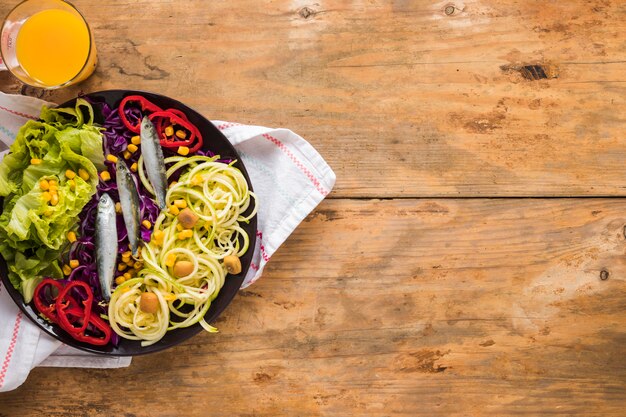 Elevated view of fresh salad with raw fish; juice and napkin on wooden table