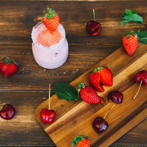 Elevated view of fresh smoothie near cherries and strawberries on cutting board