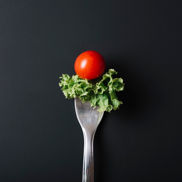 Elevated view of fresh tomato and lettuce with fork on black surface